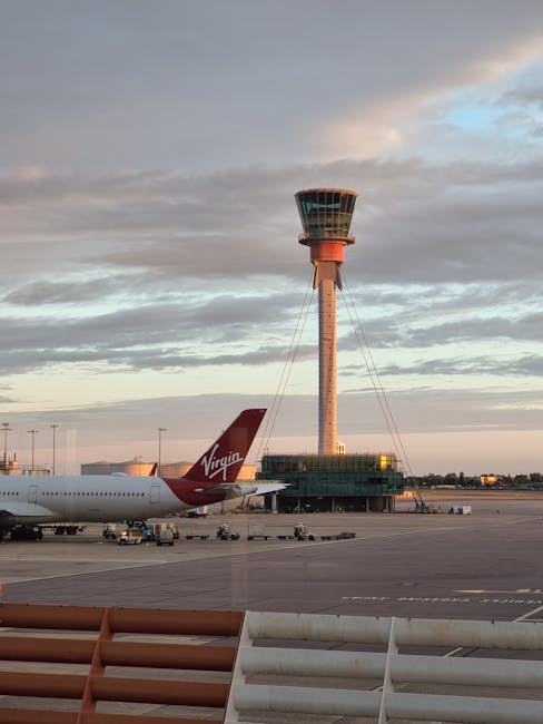 An aerial view of Heathrow Airport showing multiple airplanes parked at the terminal gates, connected by jet bridges, with some aircraft positioned on the tarmac. The airplanes are primarily white wit